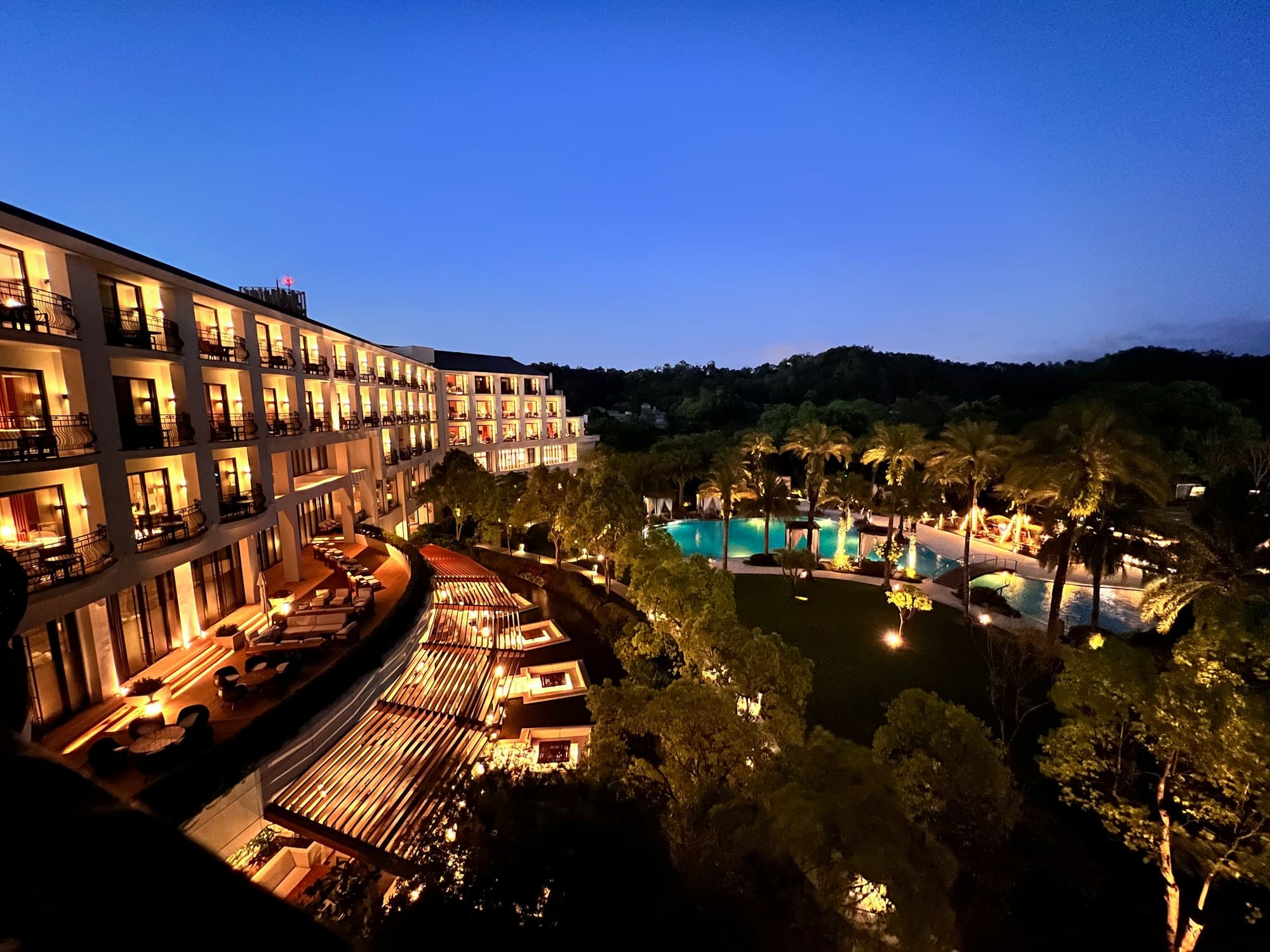 Resort terraces and pool surrounded by palms and garden lighting at dusk